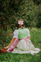 Beautiful woman picking up ripe red apple fruits in green garden. Girl in cute long peasant dress. Organic village lifestyle, agriculture, gardener occupation. High quality
