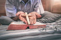 a man in bed holding a cross over a Bible 