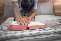a man kneeling  on a bed with a Bible 
