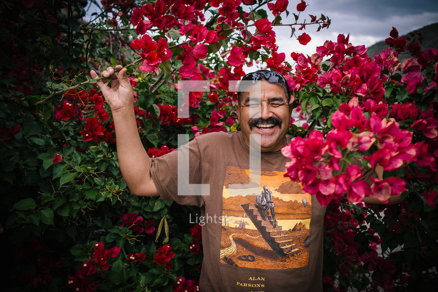 A smiling man standing among flowering bushes.