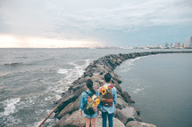 a couple standing on a jetty with flowers in their bags 