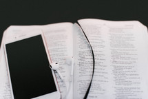 iPhone and earbuds on the pages of a Bible 
