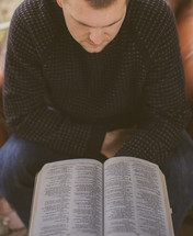 A young man sitting in a chair reading a Bible
