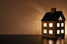 glowing light from a candle holder in the shape of a house 