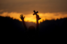 Silhouette of young male christian standing and holding a cross 