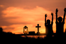 two boys with hands raised at sunset 