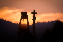 silhouette of a young man holding up a Bible and cross in worship at sunset 