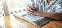 Close up of the hands of a boy over a holy bible praying.