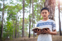 a teenage boy praying in a forest 