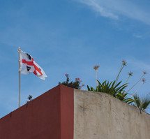 flag of Sardinia (aka flag of the Four Moors) on the top of a wall, over blue sky