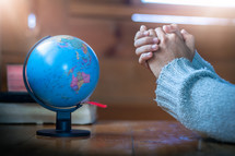 praying hands beside of a globe 