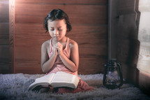 a little girl reading a Bible and praying 