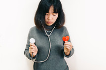 a woman holding a stethoscope and a broken red paper heart 