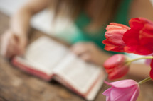 Woman reading the Bible on a table with tulips.