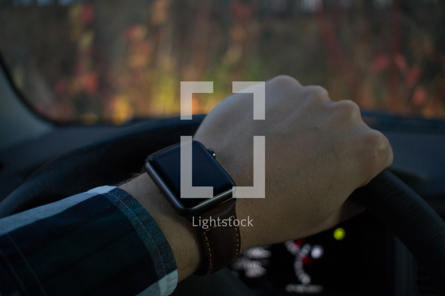 smartwatch on the wrist of an man behind a steering wheel driving 