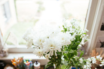 flowers in a vase on a desk in front of a window 