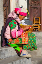 Woman in traditional Chinese minority tribe clothes sewing whilst sitting on stairs