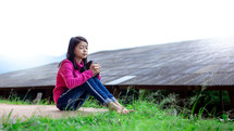 a girl sitting outdoors praying holding a Bible 