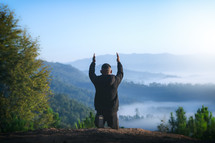 man kneeling in prayer on a mountaintop 