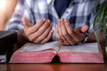 lifted hands over an open Bible 