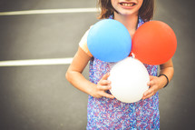 girl child holding patriotic colored balloons 
