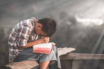 a boy praying outdoors over a Bible 