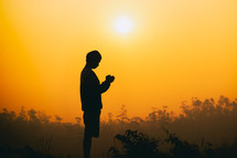 silhouette of a young man with praying hands 