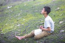 a child sitting on a hill praying 