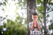 a boy reading a Bible outdoors by a tree 