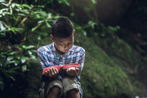 a little boy sitting in a forest reading a Bible 