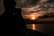 a man taking a picture of the sun at sunset over the ocean 