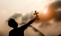 silhouette of a boy holding a cross outdoors 