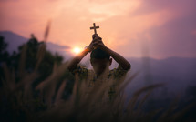 a boy holding a cross praying at sunset 