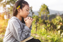 a little girl looking up to God and praying outdoors 
