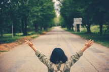 a woman with arms raised standing in the middle of a road 