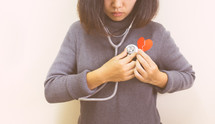 a woman holding a stethoscope and a broken red paper heart 
