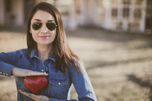 A young woman in sunglasses holding a red heart
