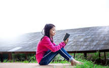 a girl sitting outdoors reading a Bible 