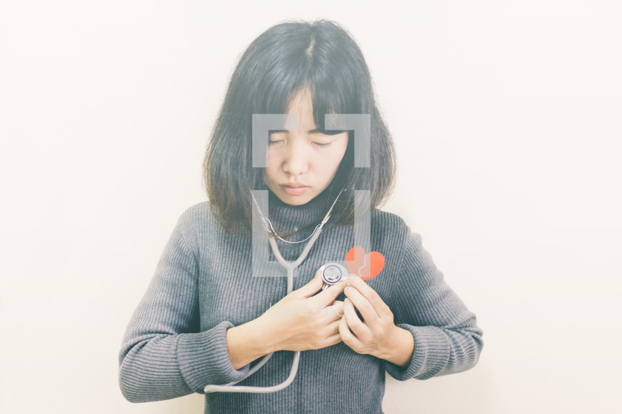 a woman holding a stethoscope and a broken paper heart 