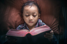 a child reading a Bible in bed 