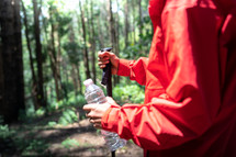 Hiker man holding bottle of water and hiking poles in forest