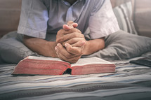 praying hands over a Bible in bed 