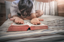 a man kneeling  on a bed with a Bible 