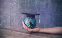a globe with a graduation cap in a cupped hand 
