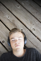 Teenager listening to music and lying down on wooden background