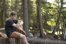 Teenager sitting on log in woods and praying with head down