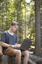 Teenager working on laptop computer in rural wooded environment in woods