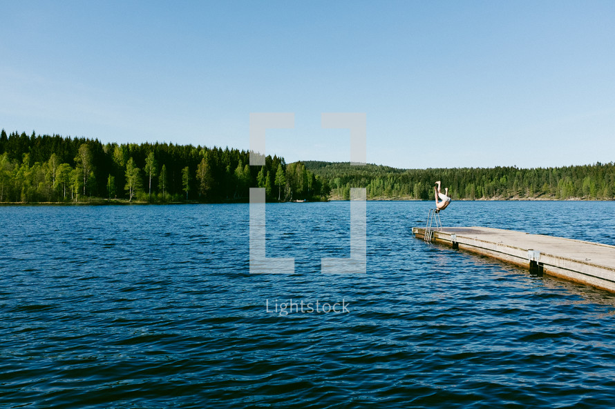 a man doing a flip off a pier into a lake 
