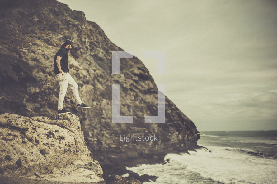 a man balancing on the edge of a rock cliff near the ocean 