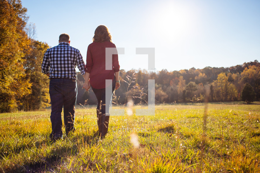 Couple walking through a field with fall foliage.